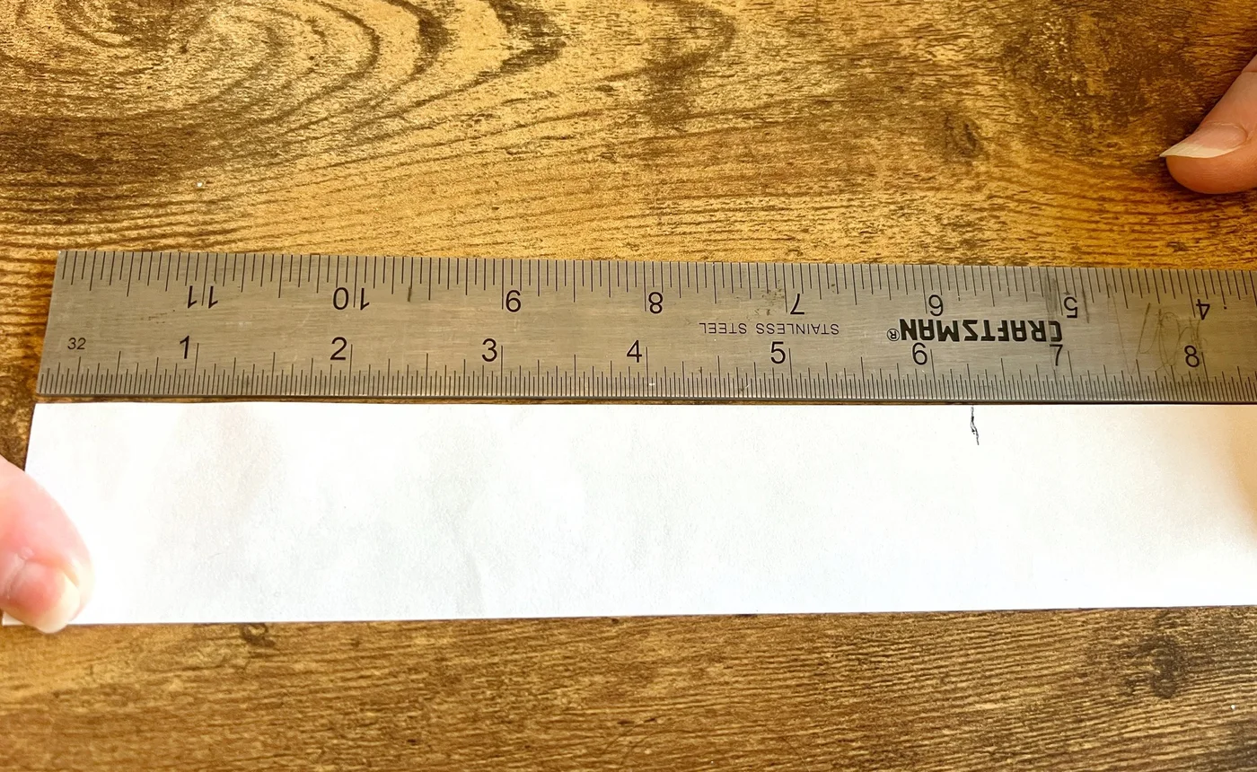 A marked strip of paper laid flat beside a ruler
